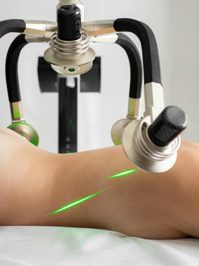 Crop anonymous topless female patient lying under green lasers of modern fat loss machine with heads in light medical clinic