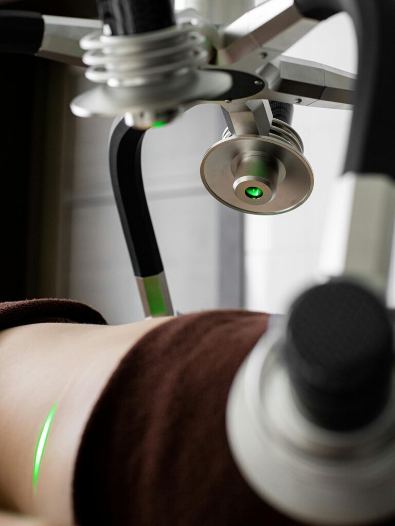 Crop unrecognizable patient lying under green lasers of contemporary weight loss machine with heads during slimming treatment in light modern medical clinic